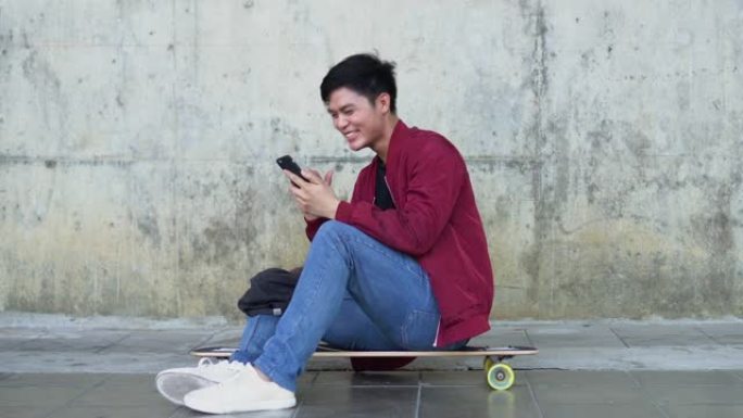 坐在滑板上使用智能手机玩社交媒体应用程序或观看娱乐媒体或在户外公园与朋友聊天的场景青少年生活概念
