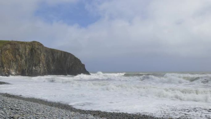 岩石海滩，海浪非常猛烈，大悬崖，天空多云。库珀海岸，沃特福德。爱尔兰