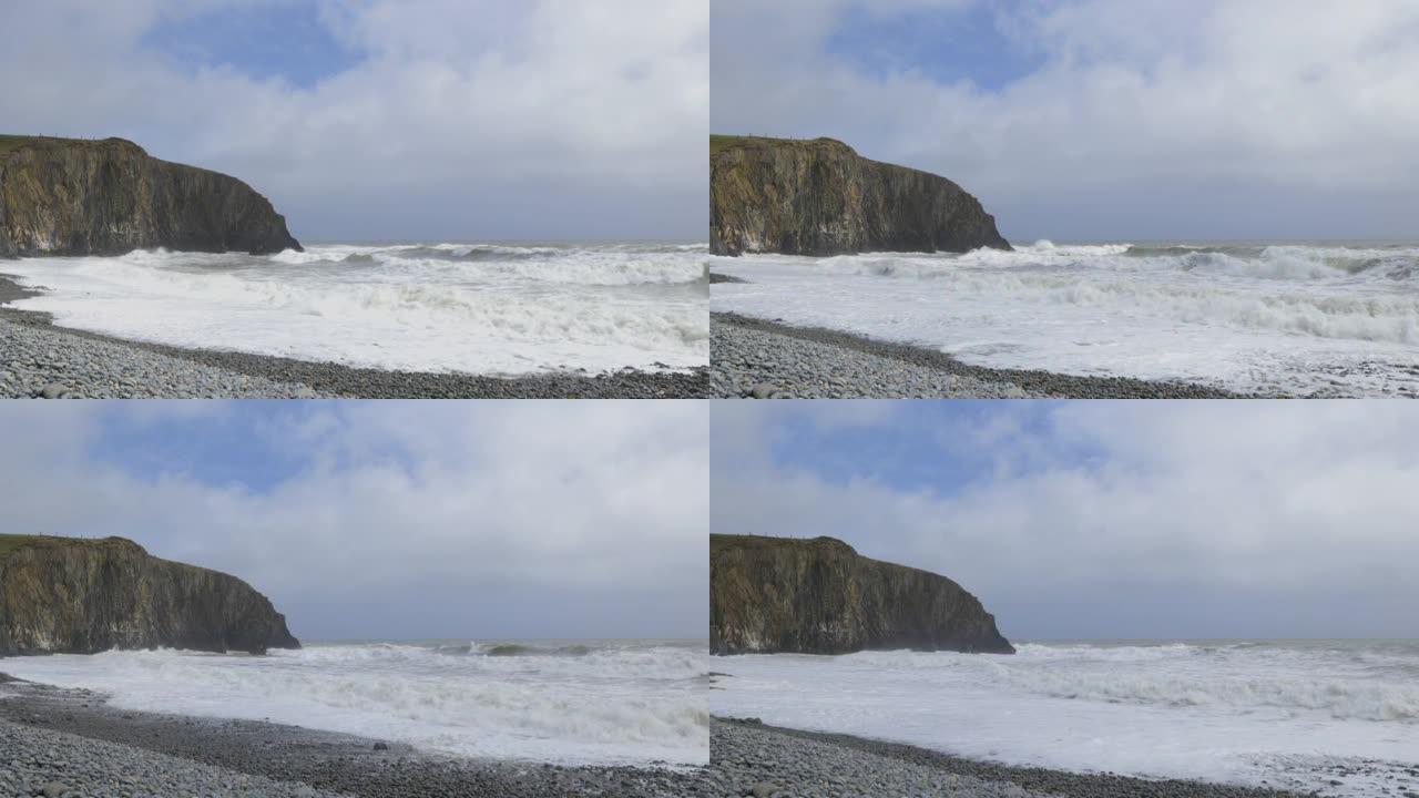 岩石海滩，海浪非常猛烈，大悬崖，天空多云。库珀海岸，沃特福德。爱尔兰