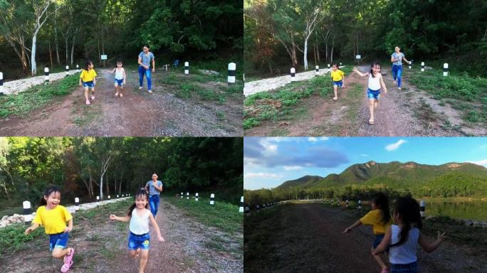 快乐的家庭在夏日公园奔跑。日落时分，母亲和孩子们沿着道路奔跑。一家人一起度假。