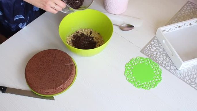 女人把花生和巧克力加到容器里。制作花生和草莓巧克力蛋糕奶油。烹饪的配料放在桌子上。