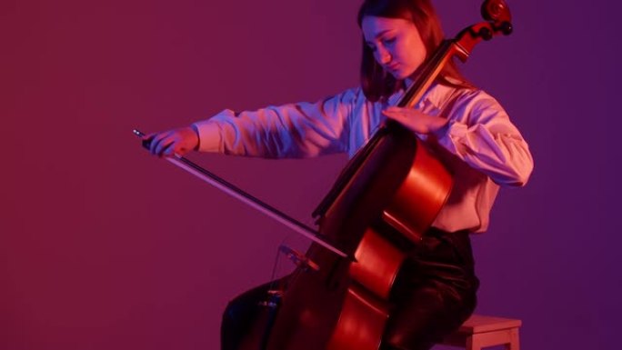 穿着紫色背景的白衬衫的黑发女孩演奏大提琴，享受音乐。音乐创造力的概念