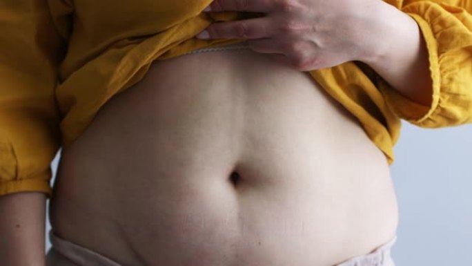超重大码女人在灰色背景上触摸她肥胖的腹部