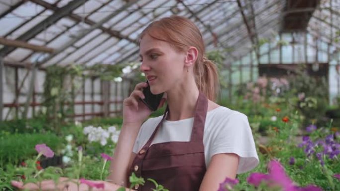 美丽快乐的女花店店长与客户在手机上谈论植物的特写肖像。白人妇女在自己的花店工作，并在智能手机上讲话。