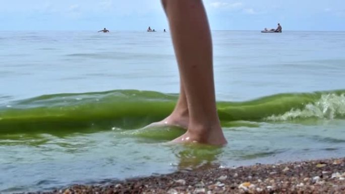试图在海里洗澡的孩子。用脚在海里试水温的人。女孩在海里洗澡前用脚摸水。十几岁的腿出海了。