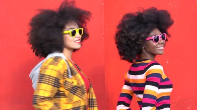 4k视频美丽的非洲裔美国妇女，非洲头发，太阳镜和彩色衣服在红色背景前微笑