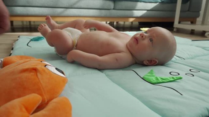 可爱的男婴躺在婴儿活动健身房玩垫子和他的父亲玩耍，婴儿感官发育，3个月大的新生婴儿在客厅地板上