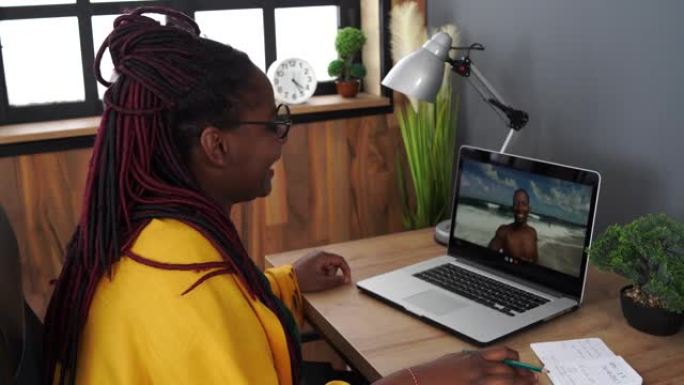 4k视频开朗的年轻的非洲裔美国妇女，戴着眼镜，用笔记本电脑进行视频通话，并与一名非洲裔美国男子交谈