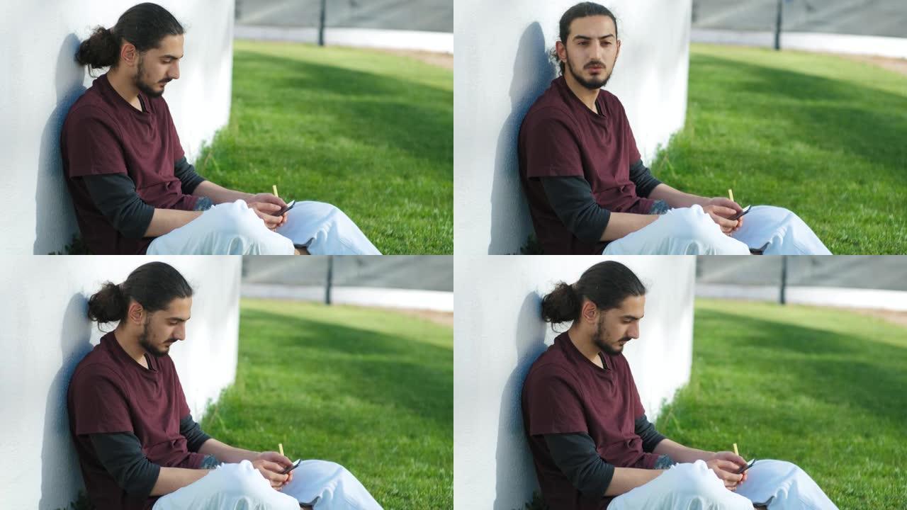 年轻迷人的阿拉伯男子坐在公园里，使用智能手机