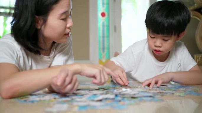 亚洲家庭，母子躺在地板上做拼图游戏。女人拍手，男孩微笑。在家工作期间家庭幸福。女人教孩子解谜。开朗的