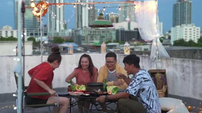 多元化的亚洲成人朋友一起在户外屋顶享受晚宴，提供食物和饮料