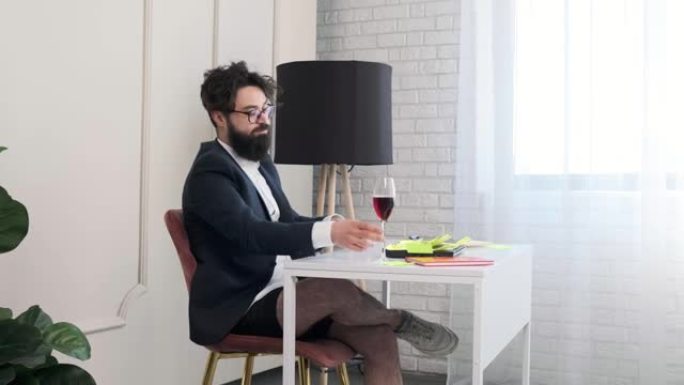 没有裤子的大胡子男人合上电脑，享用一杯葡萄酒