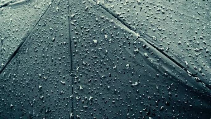 黑色雨伞上的雨滴。极端特写。雨滴落在阳伞上。抽象纹理模式。雨季自然背景镜头。选择性聚焦。浅景深。复制