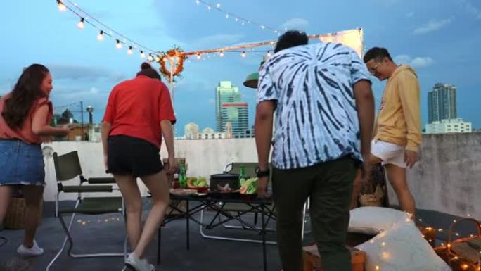 多元化的亚洲成人朋友一起在户外屋顶享受晚宴，提供食物和饮料