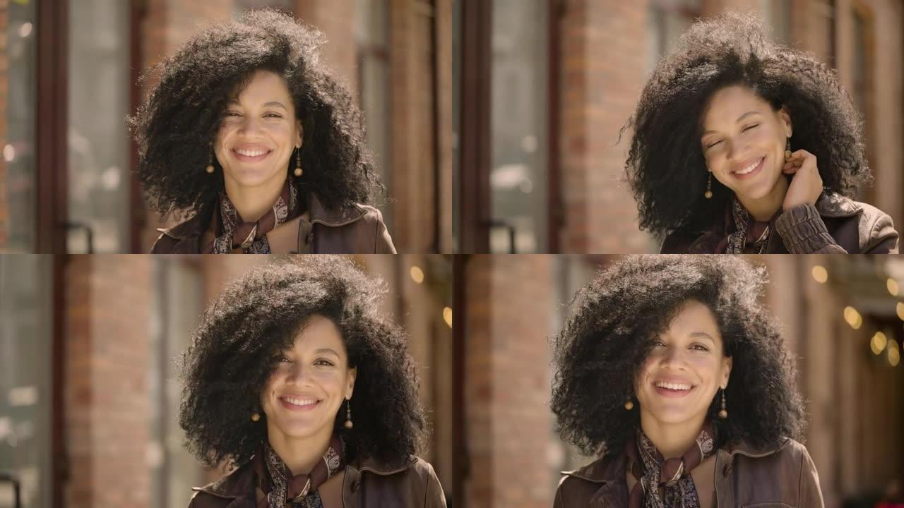 年轻的非洲裔美国妇女看着相机微笑的肖像。穿着棕色皮夹克的黑发女人在模糊的建筑背景下摆姿势。特写。慢动