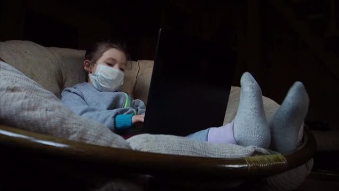 快乐的孩子在医疗面具在笔记本电脑键盘上打字，有趣的踢腿。