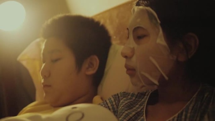 亚洲儿童晚上在家一起在床上用数字平板电脑看电影，女孩用面膜遮住脸，生活方式理念。