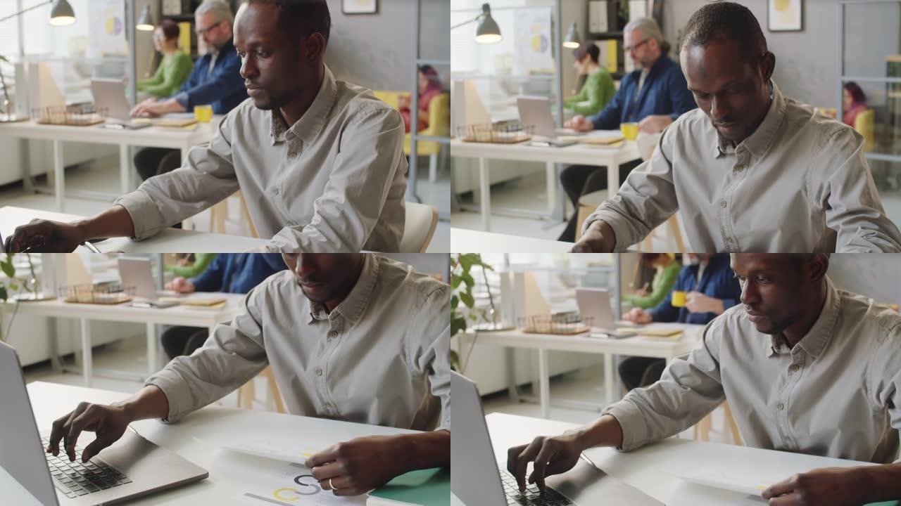 非裔美国人在办公室使用笔记本电脑并阅读文档