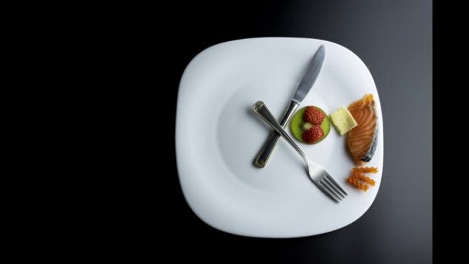 用叉子和刀子的手模拟时钟的盘子显示食物，间歇性禁食的概念