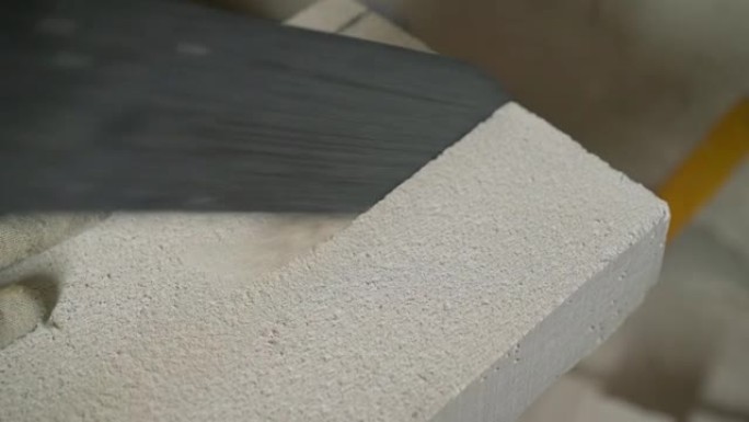 工人用手锯切割加气混凝土制成的建筑砌块。一名工人切割加气混凝土块。