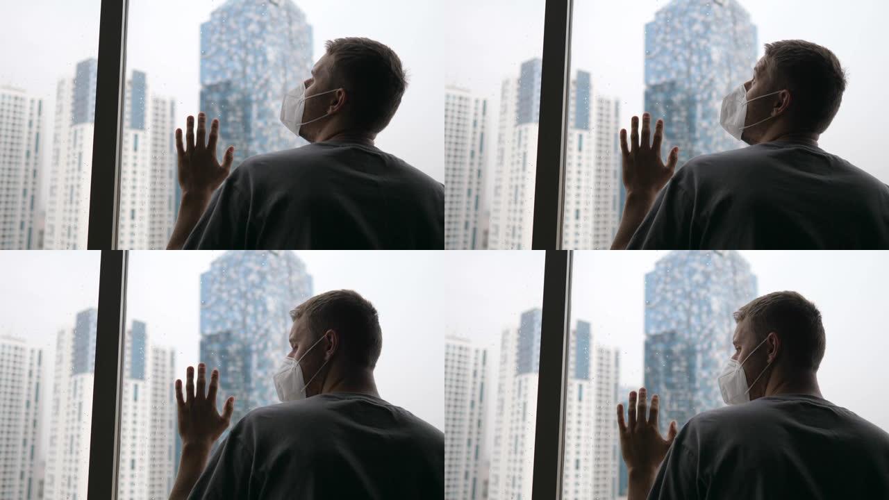 一个戴着面具的成年白人男子透过摩天大楼的窗户看。新型冠状病毒肺炎大流行引起的抑郁症