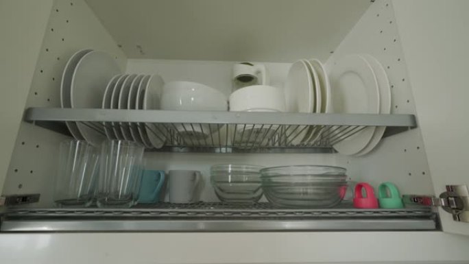 男人打开厨房用干净的餐具关闭橱柜，白色的盘子和杯子在厨房里晾干。