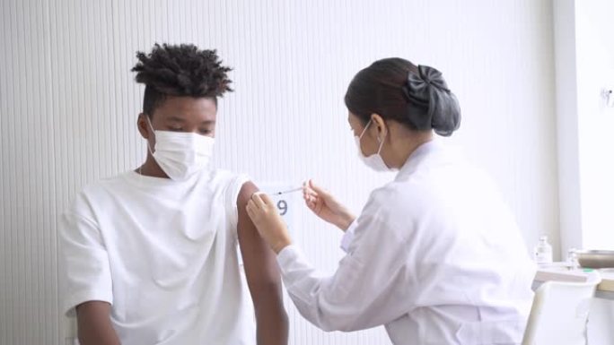非裔美国男子在诊所或医院接种covid疫苗时看着的肖像，手持护士注射疫苗以获得免疫力以保护病毒。戴着