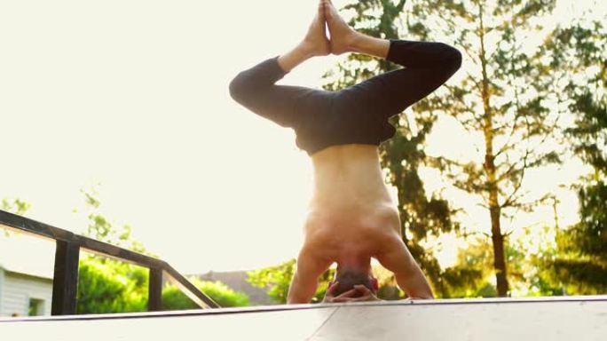 裸胸瑜伽行者在夏季公园练习瑜伽。人头朝下站着。自我保健教育