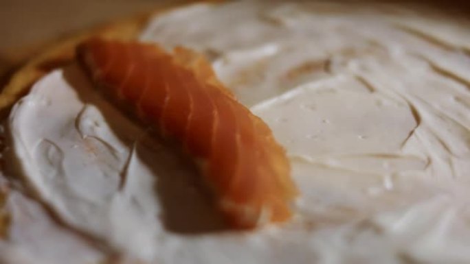 薄薄的美味彩色煎饼。女人的手将鲑鱼片放在木板上涂有奶油奶酪的黄色煎饼上的宏观视图。4k视频。