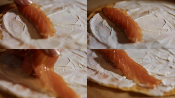 薄薄的美味彩色煎饼。女人的手将鲑鱼片放在木板上涂有奶油奶酪的黄色煎饼上的宏观视图。4k视频。