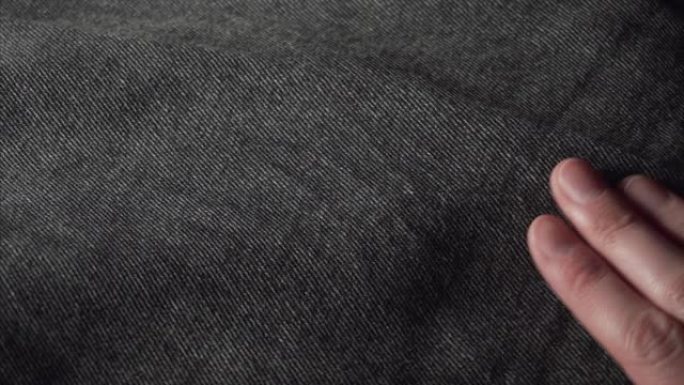 顾客在服装店或纺织厂触摸一条光滑的黑色牛仔裤，检查布料的质量