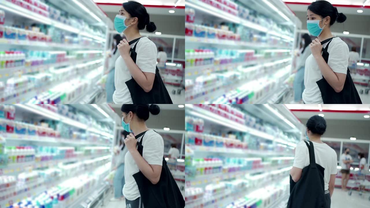 2019冠状病毒病大流行期间，在食品零售商店，亚洲女性看着冰箱货架。小姐食品检疫储备，消费者选择选择