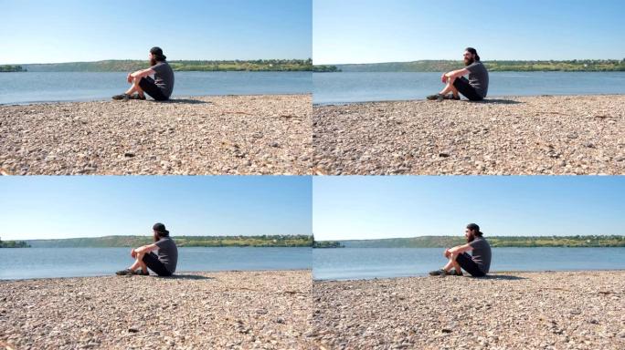 4k的镜头，男人坐在湖或河附近，欣赏美景。