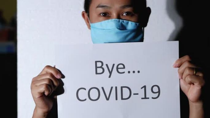 光照耀着亚洲女人，拿着一张标有Bye COVID 19的纸，站在白色背景上。为电晕病毒大流行说再见的