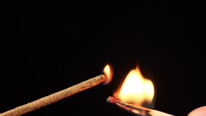 黑色背景上带有熏香的燃烧棒，从木制火柴着火