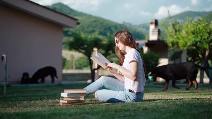 沉思的女学生坐在房子附近的草地上看书和阅读故事。集中女孩阅读书籍，翻页和分析信息。户外考试准备