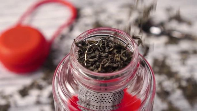绿茶。干燥的卷叶落入玻璃茶壶特写。