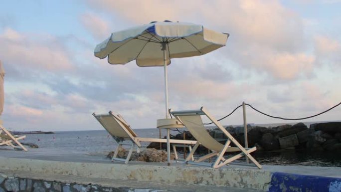 日落时分，两把躺椅和一把太阳伞在海边的岩石上