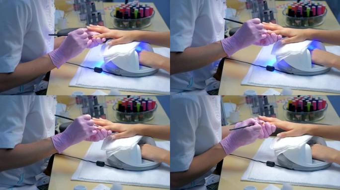 美甲师大师画客户的指甲凝胶虫胶，另一只手在紫外线灯。