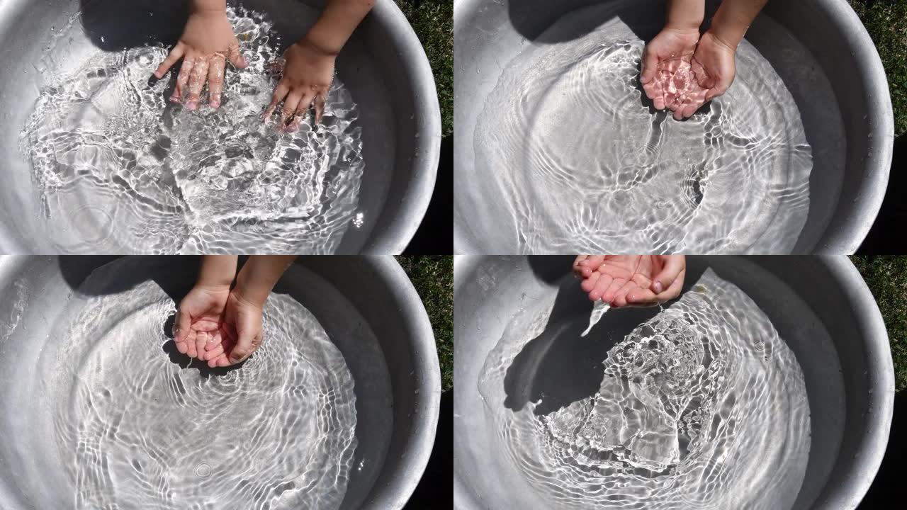 孩子在盆子里的清水里洗手。夏季乐趣