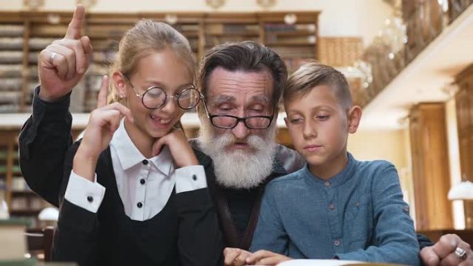 英俊的大胡子老人看书，举起手指，让他十几岁的孙子明白书的内容