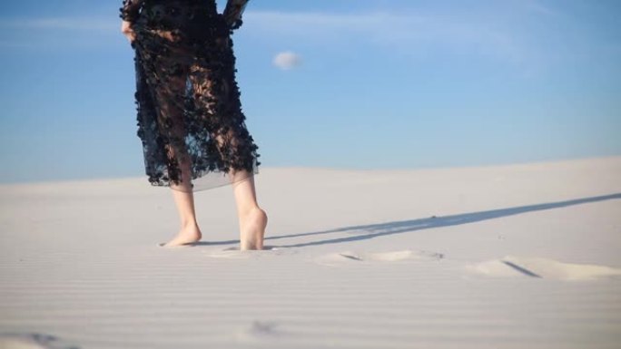 女人的腿赤脚在沙漠中留下的脚印在白沙上。