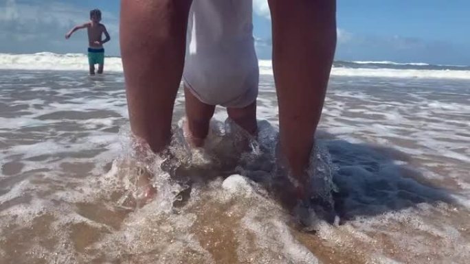 可爱的婴儿赤脚在海滩上，海浪在岸边撞击。幼儿感受海水