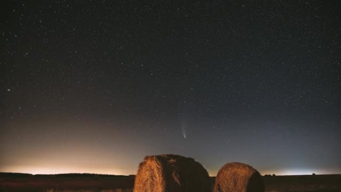 彗星Neowise C/2020 F3在夏季农田干草堆上方的夜星天空。收获后，夜星在乡村景观之上，干