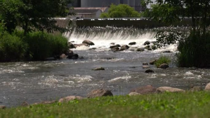 在威斯康星州一个人造的河坝的背景下，从河岸上的草开始向谷物升降机或筒仓平移。