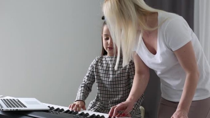 小女孩在线看音乐课，在家学习。小女孩在视频通话后看着电脑屏幕，一边练习钢琴技巧。