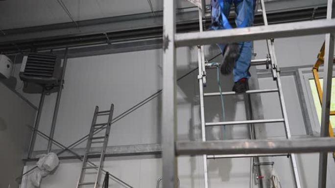 戴着安全带和安全帽的建筑工人从脚手架上从高高的梯子上下来。