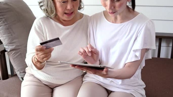 亚洲妇女教老年人使用信用卡和平板电脑进行在线购物