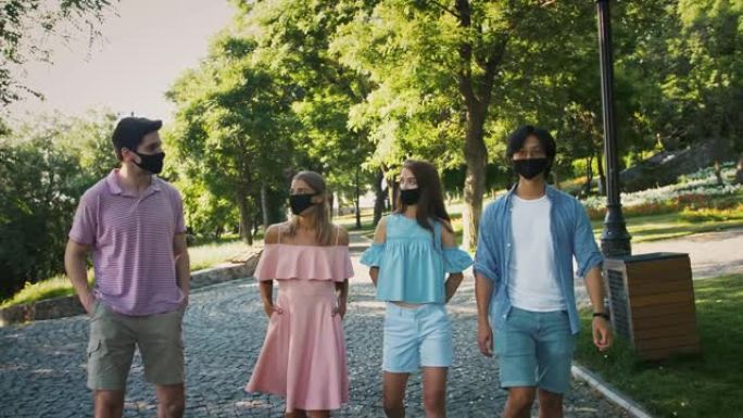 戴着黑色防护面具的年轻朋友正在绿色景观公园聊天和散步。晴天。新型冠状病毒肺炎，冠状病毒大流行