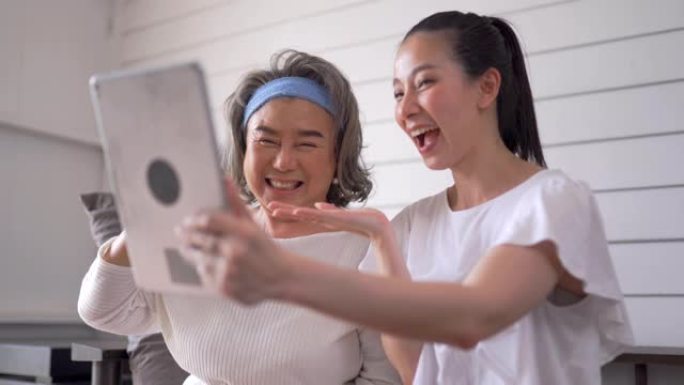 亚洲高级妇女和女儿在家使用平板电脑进行视频会议